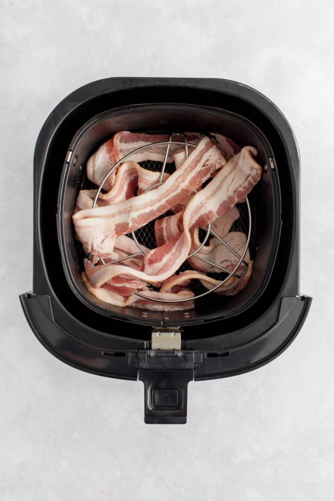 Bacon in an air fryer basket with a rack.