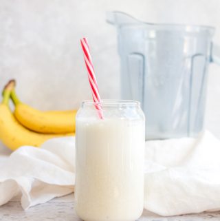 Banana milk in a cup with a red and white straw.