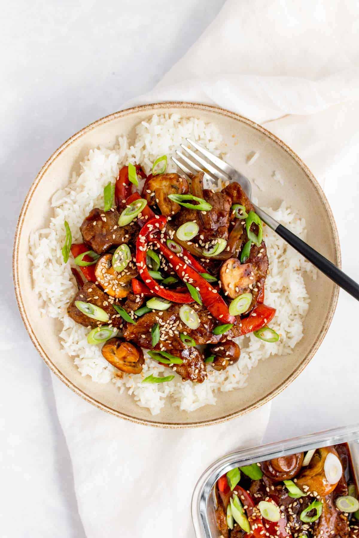 A plate of rice with black pepper beef and green onions with a fork inside.