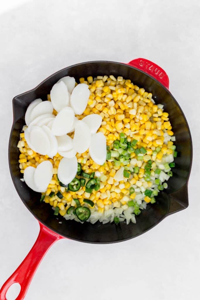 Corn, green onions, jalapeno, rice cakes added to the skillet with onions.
