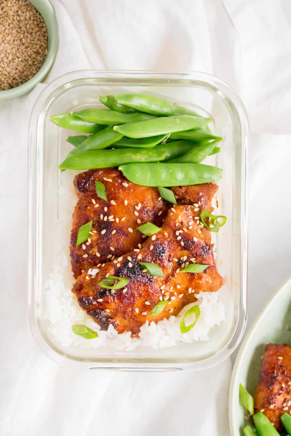 Meal prep container with rice, Korean chicken thighs, and snap peas.