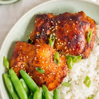 Close up of two Korean chicken thighs with snap peas in a plate.