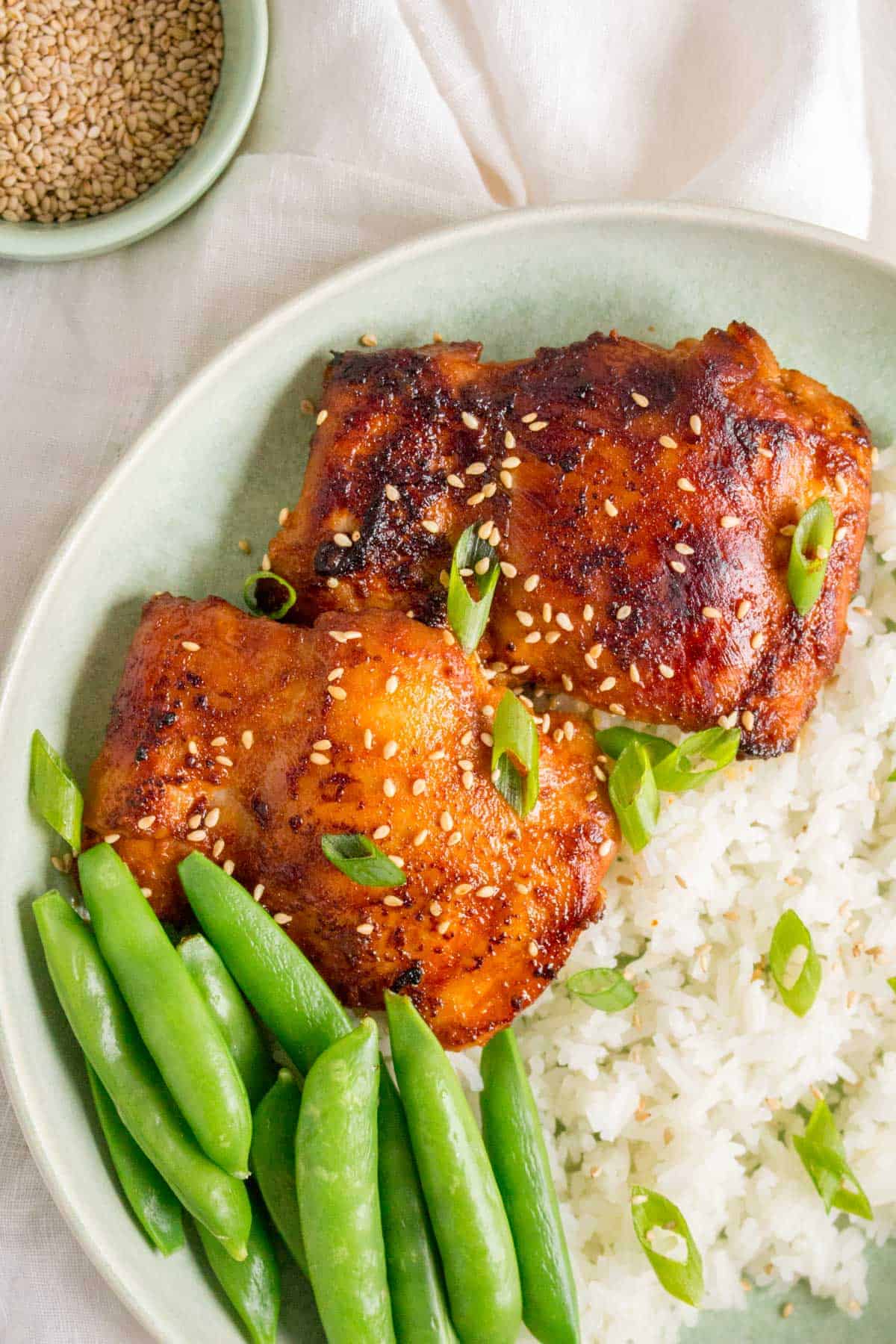 Close up of two Korean chicken thighs with snap peas in a plate.