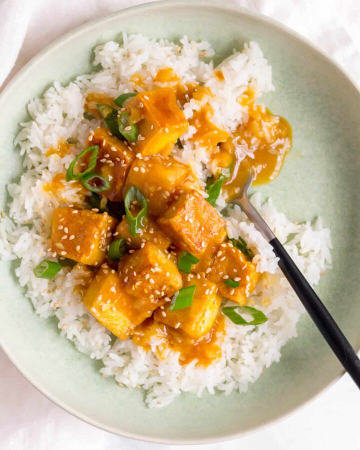 Saucy orange tofu over top of rice with a fork.