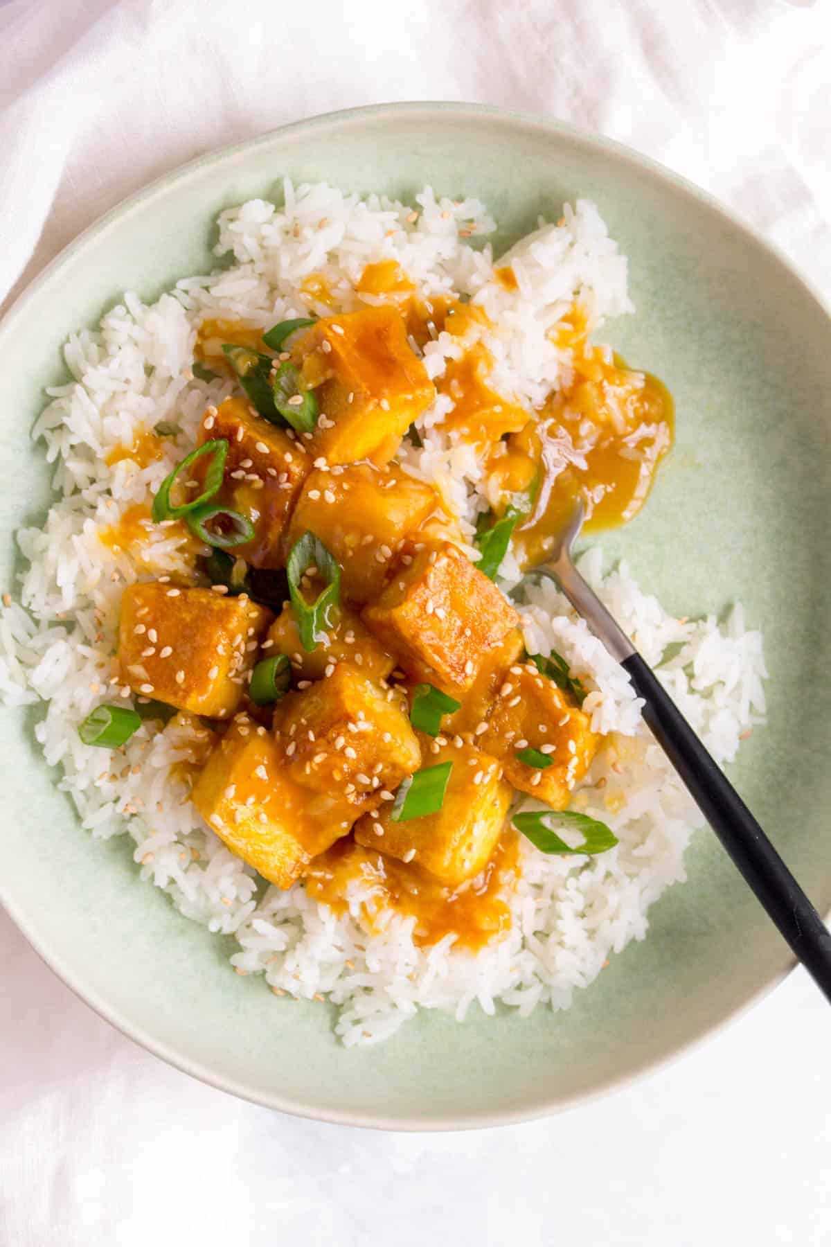 Saucy orange tofu over top of rice with a fork.