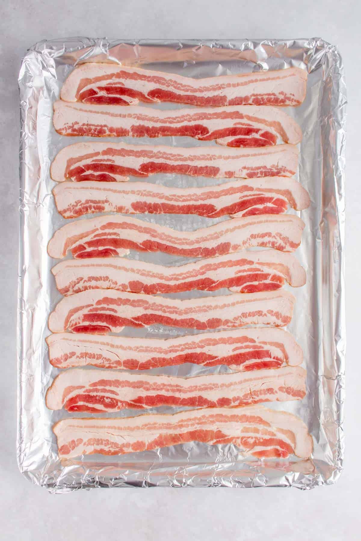 Ten strips of bacon on a lined sheet pan.
