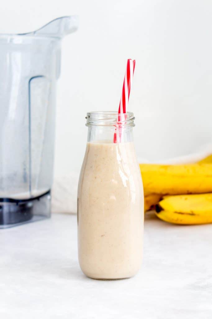 Roasted banana cinnamon milk in a glass with a straw with vitamix and banana in the background.
