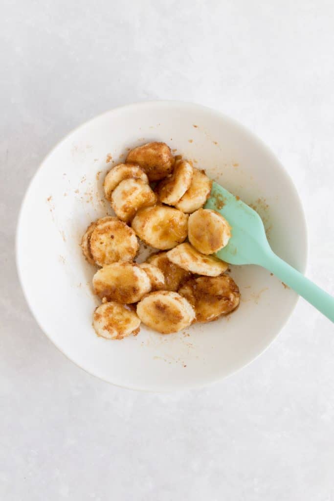 Mixing banana slices, brown sugar, cinnamon, vanilla, and salt in a bowl with a rubber spatula.