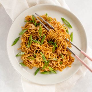 Bowl of sesame noodles topped with green onions and fried onions.