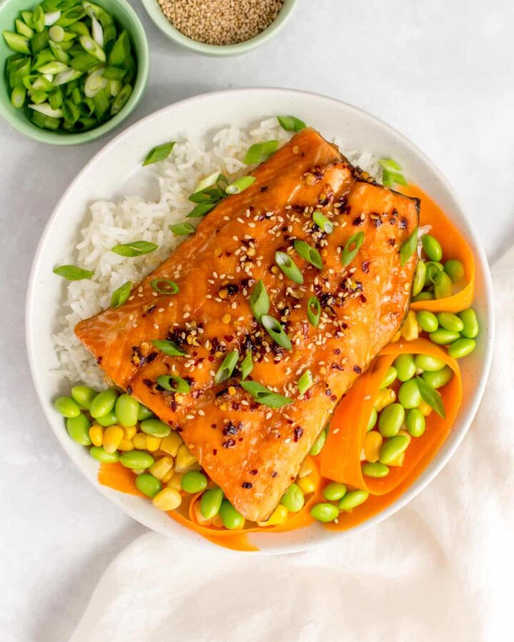 A plate with rice, corn, edamame, carrots, and sweet chili salmon.
