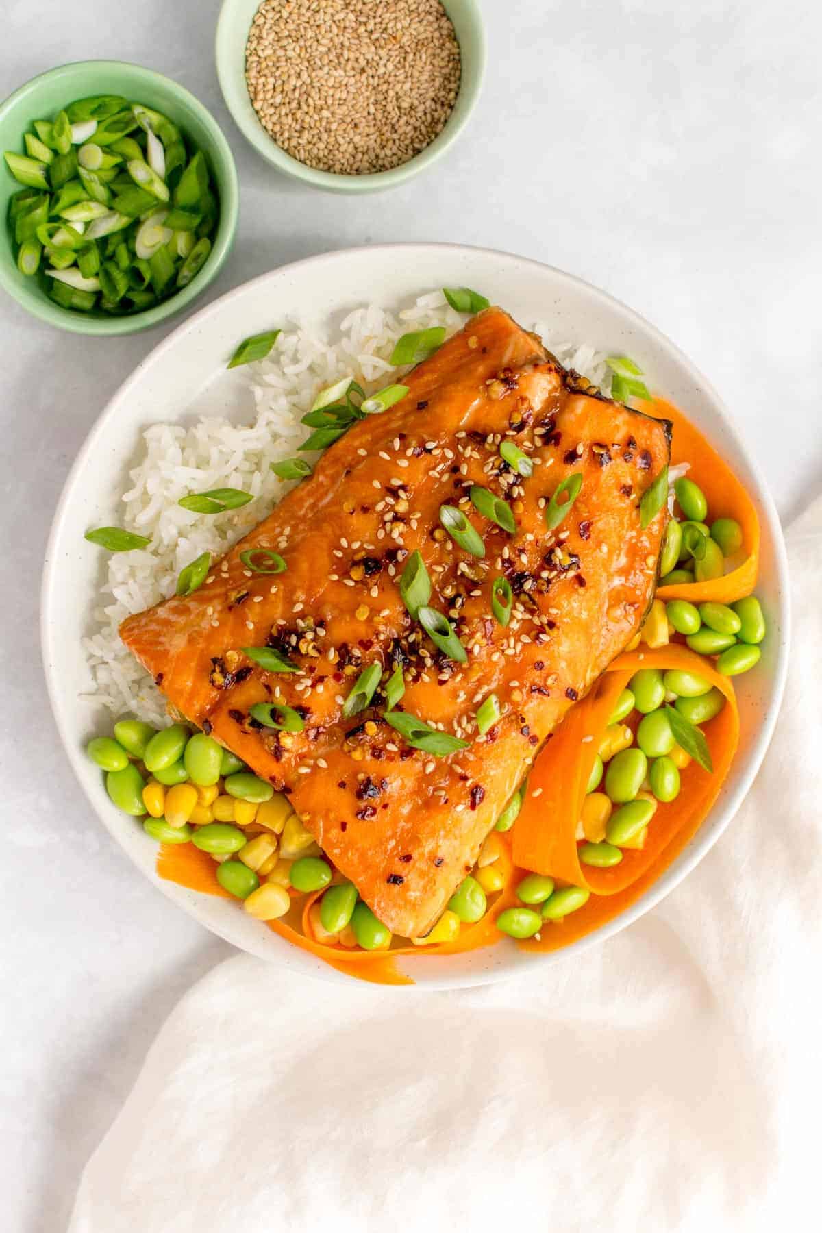 A plate with rice, corn, edamame, carrots, and sweet chili salmon.