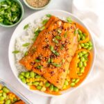 A plate with rice, corn, edamame, carrots, and sweet chili salmon on top.