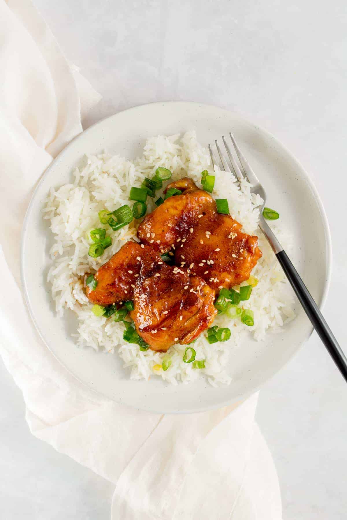 A plate with a bed of rice with green onions with two orange glazed chicken thighs on top.