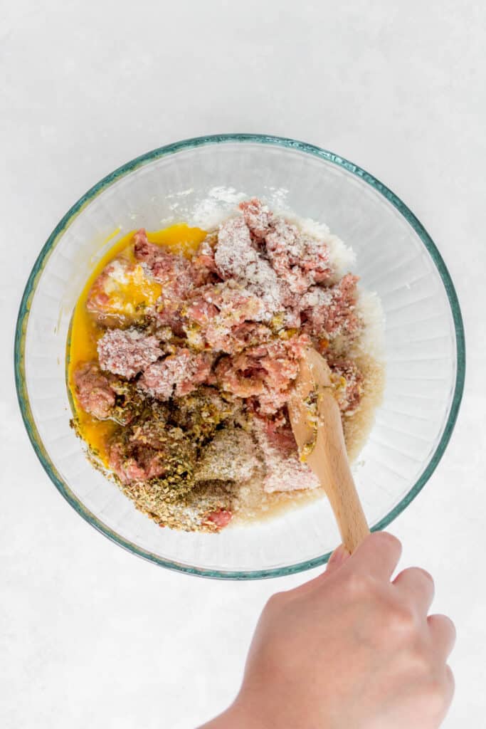 Mixing meat mixture in a bowl with a wooden spoon.