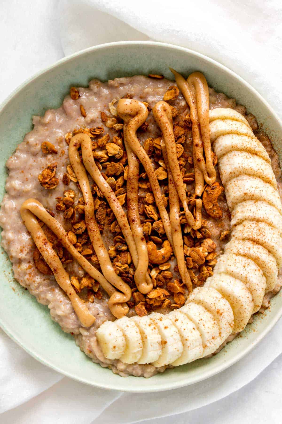 A plate of banana bread oatmeal with sliced bananas, granola, and nut butter.