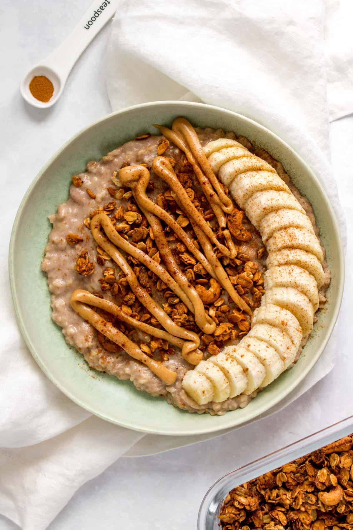 A plate of banana bread oatmeal with sliced bananas, granola, and nut butter.