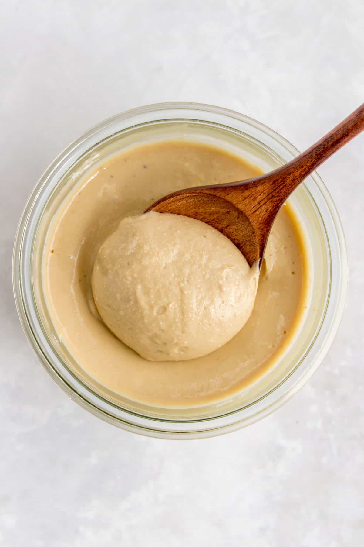 Overhead view of a wooden spoon scooped into a jar of cashew butter.