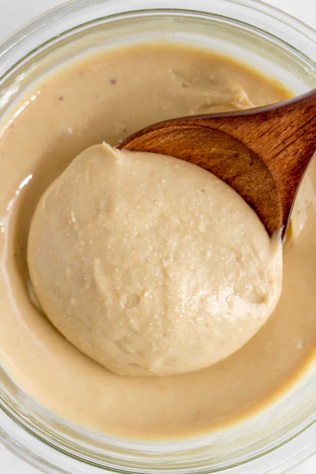 Close up of an overhead view of a wooden spoon scooped into a jar of cashew butter.