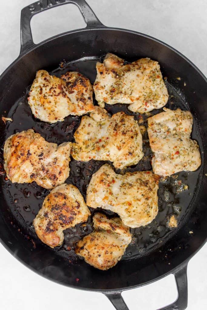 Chicken thighs seared in a pan.