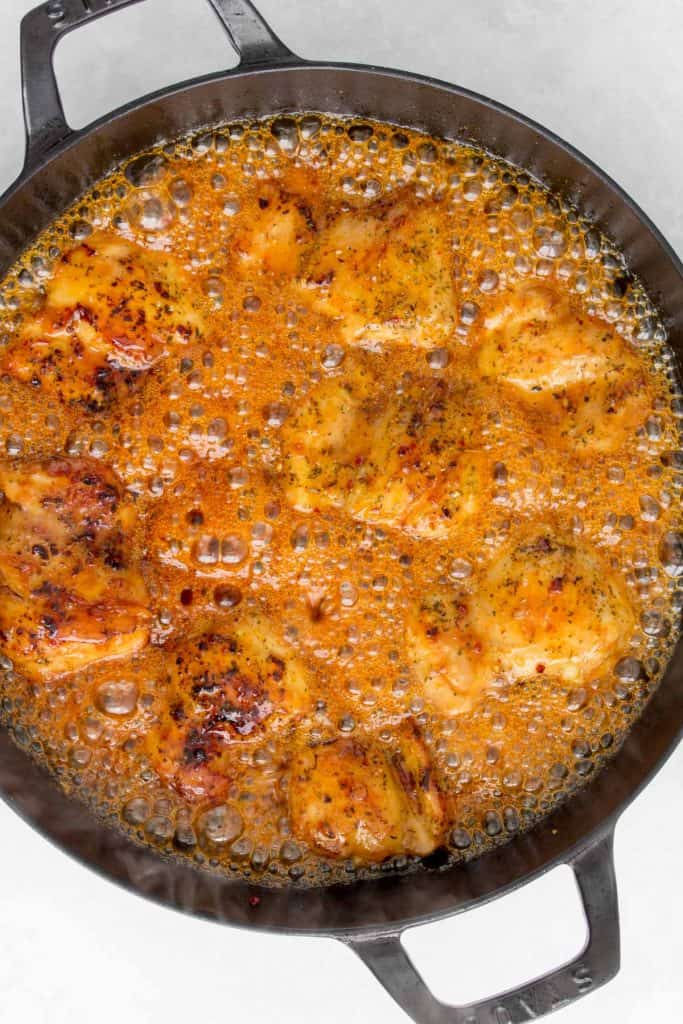 Hot honey bubbling in a pan with chicken thighs.