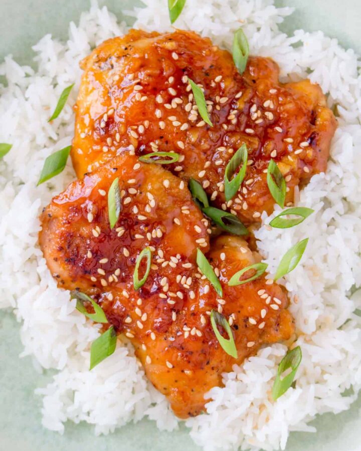 Close up of two spicy chicken thighs over rice.