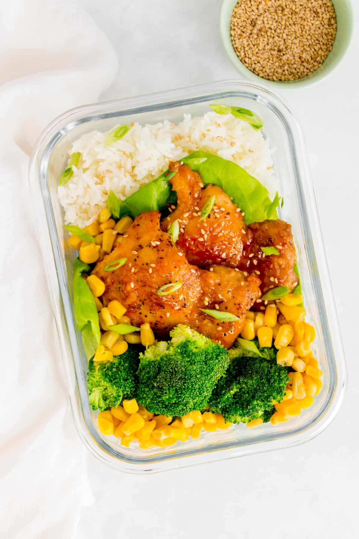 Meal prep container of chicken thighs with rice, corn, and broccoli.