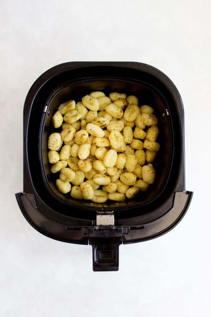 Overhead view of an air fryer basket of gnocchi before air frying.