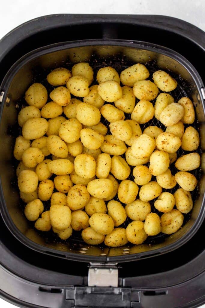 An air fryer basket with cooked gnocchi