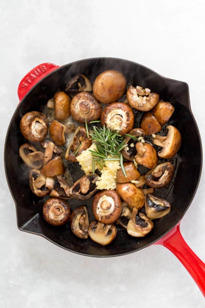 A pan with mushrooms with garlic and rosemary added.