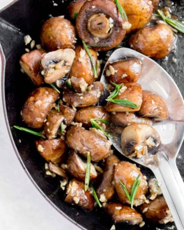 Close up of garlic butter mushrooms with rosemary in a pan.