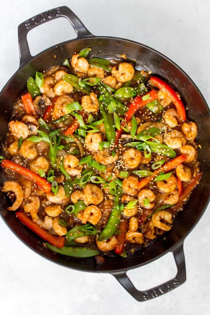 Overhead view of a pan of garlic shrimp stir fry with green onions and sesame seeds.