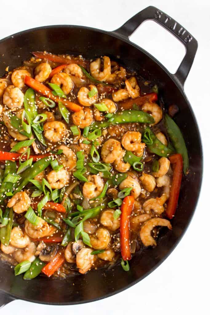 Overhead view of a pan of garlic shrimp stir fry with green onions and sesame seeds.