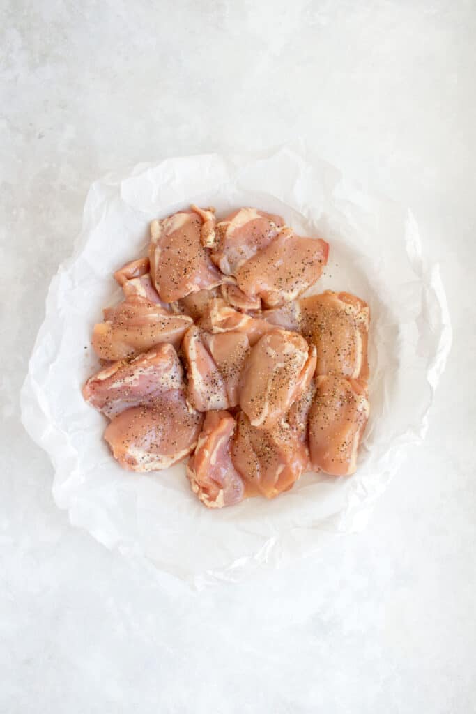 A plate of raw chicken thighs seasoned with salt and pepper.