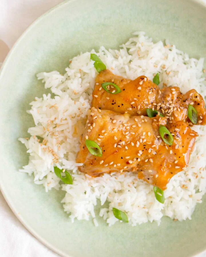 Overhead view of a plate of rice with two honey sriracha lime chicken thighs on top.