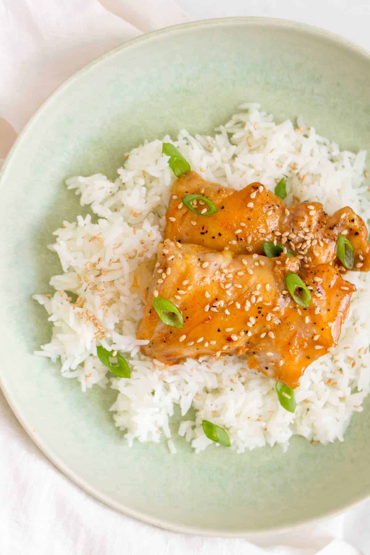 Overhead view of a plate of rice with two honey sriracha lime chicken thighs on top.