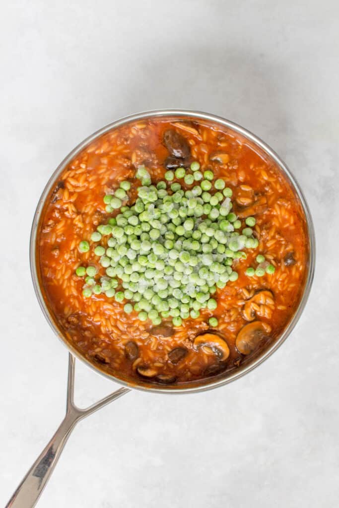 Frozen peas added to a pot of orzo bolognese