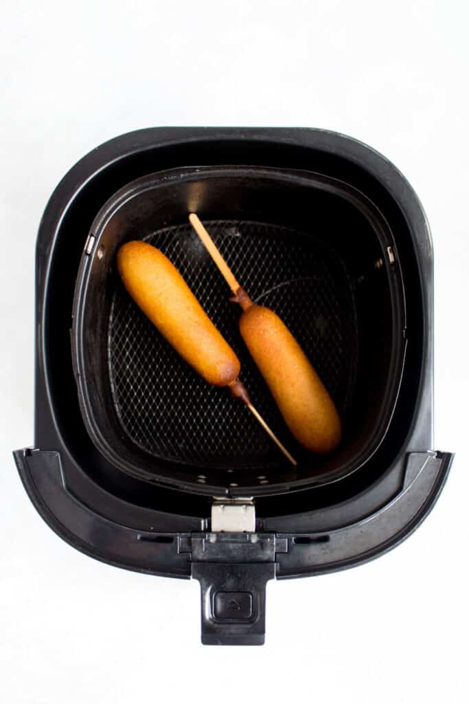 Two air fried corn dogs in an air fryer basket.