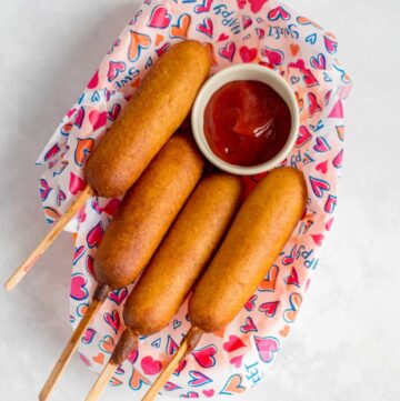 A basket of four corn dogs with a serving of ketchup.