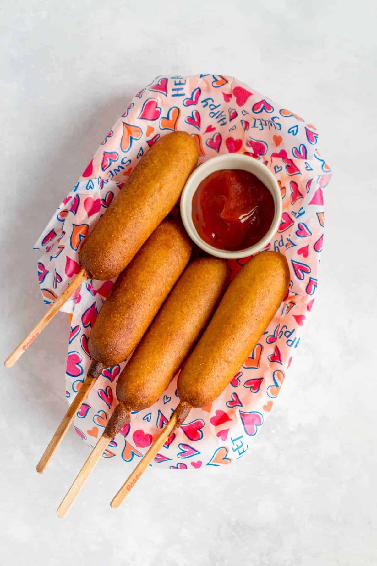 A basket of four corn dogs with a serving of ketchup.