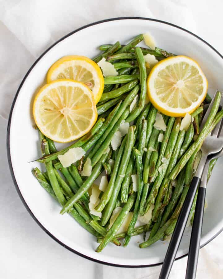 Close up of a plate of green beans with lemon slices and parmesan.