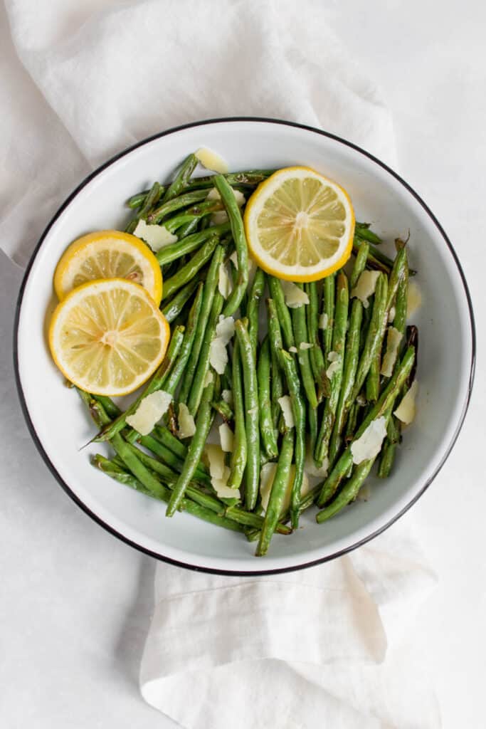 Overhead view of a plate of air fryer green beans with some parmesan on top and lemon slices.