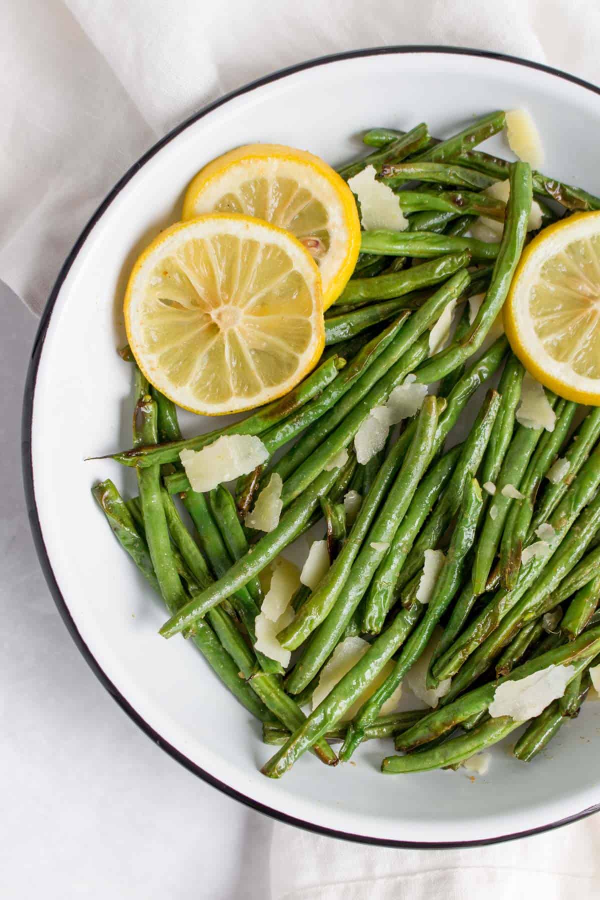 Close up image of a plate of green beans with lemon slices and parmesan with a fork and a spoon inside the plate.