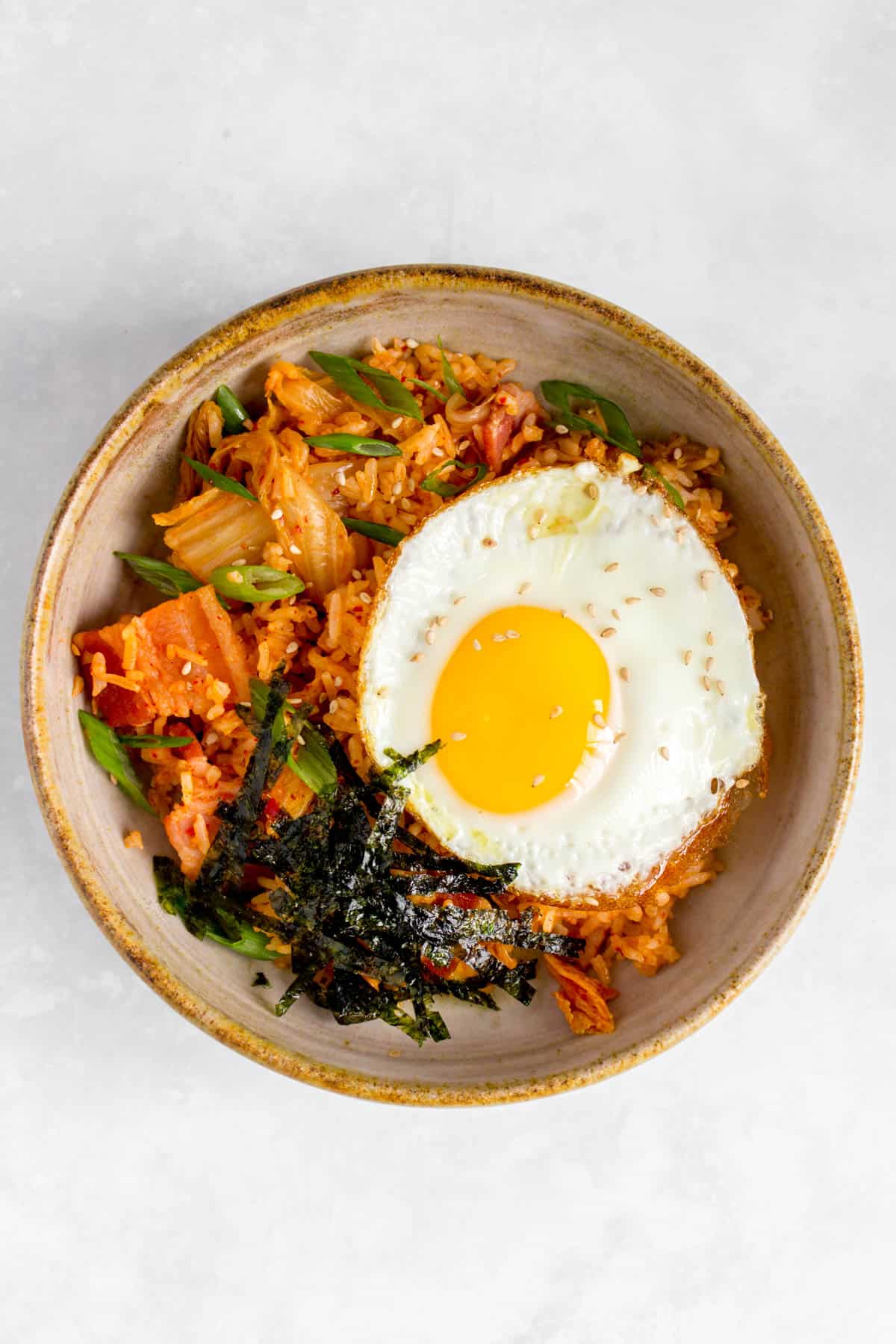 A bowl of bacon kimchi fried rice with a fried egg and shredded seaweed on top.