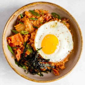 A bowl of bacon kimchi fried rice with a fried egg and shredded seaweed on top.