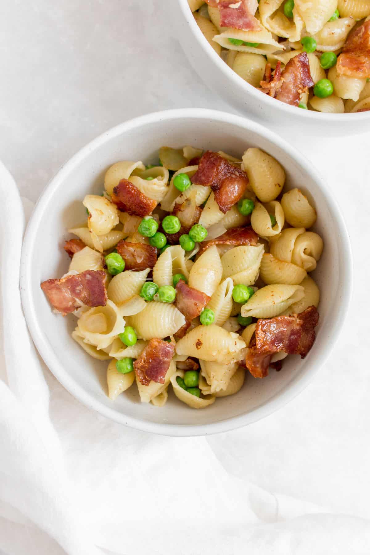 Overhead view of a bowl of pasta with peas and bacon.