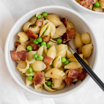 Overhead view of a bowl of pasta with peas and bacon and a fork.