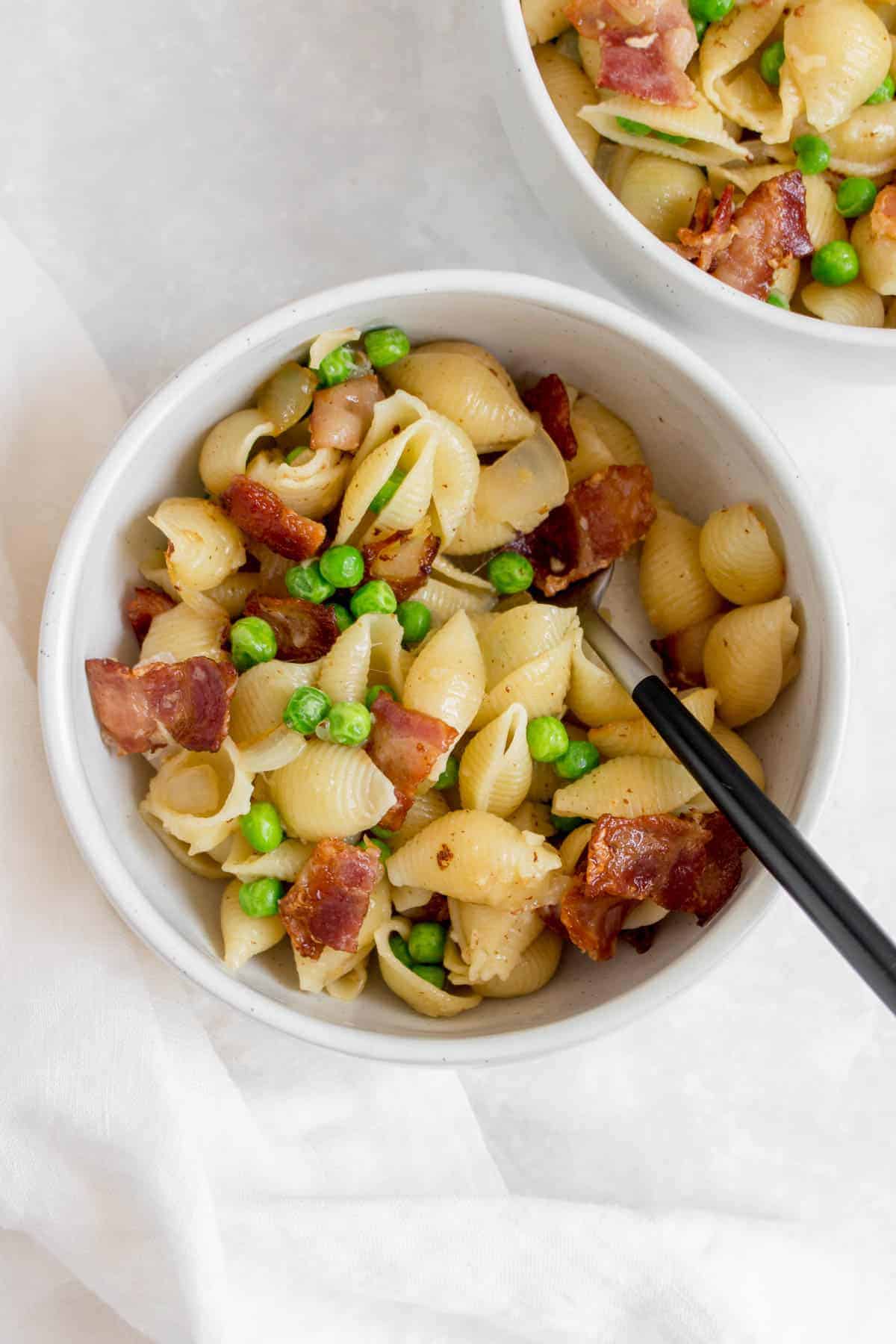 Overhead view of a bowl of pasta with peas and bacon and a fork.
