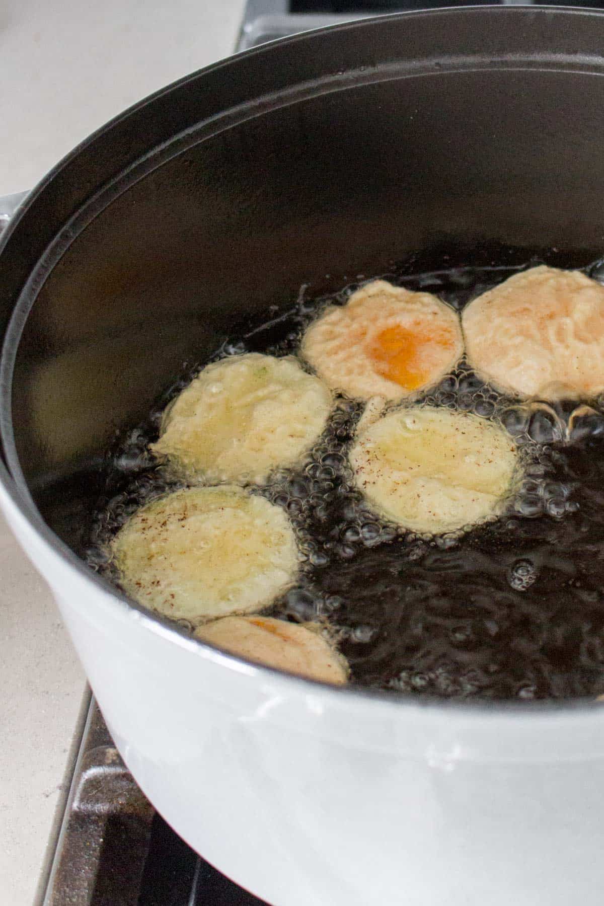 Vegetable tempura cooking in oil in a pot.