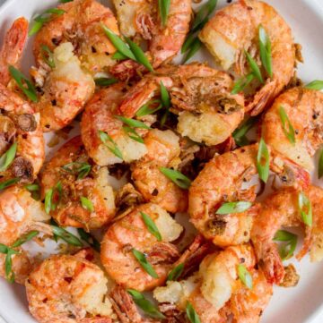 Overhead view of a plate of salt and pepper shrimp with green onions on top.