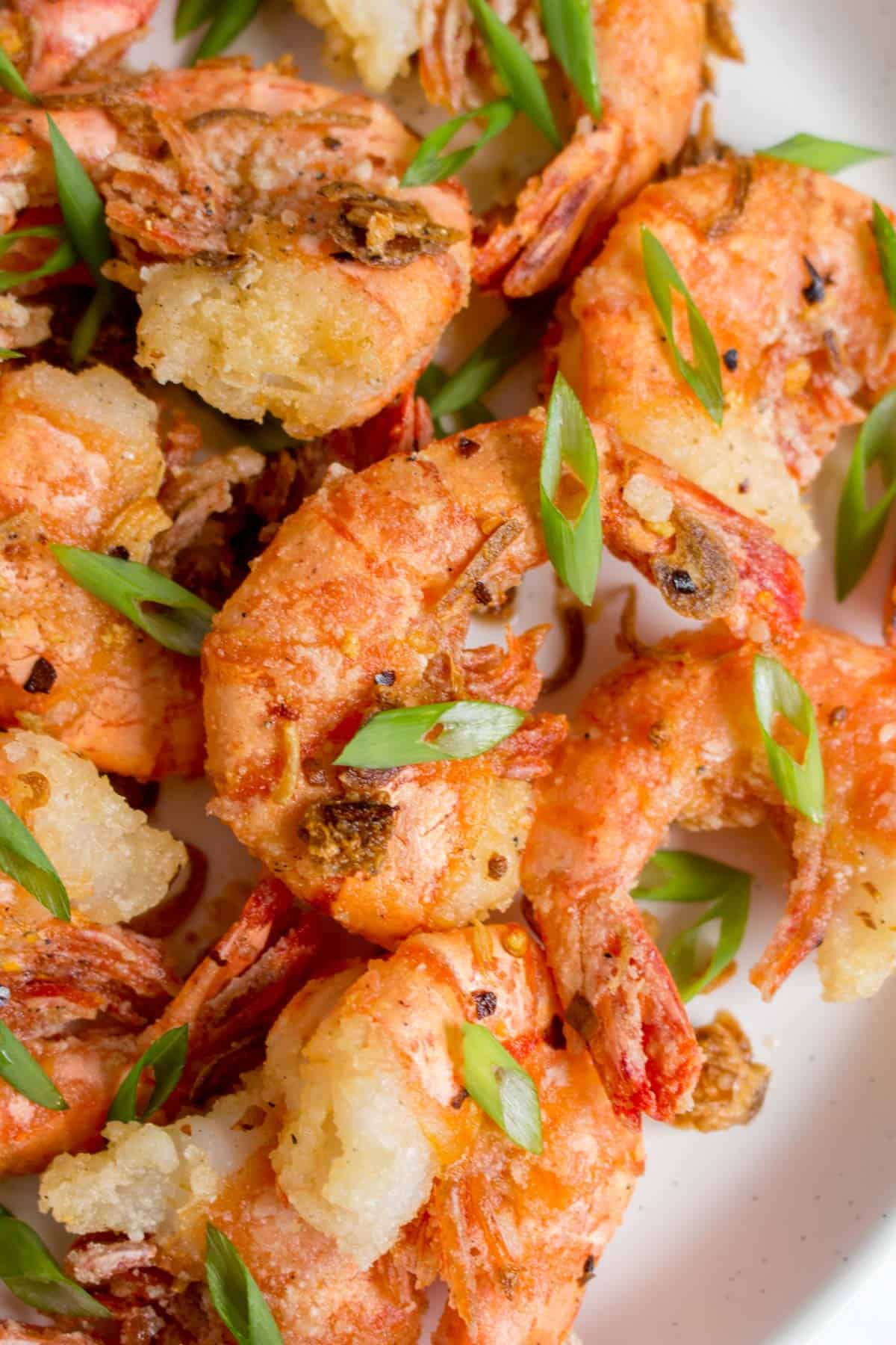 Close up of a salt and pepper shrimp with green onions on top.